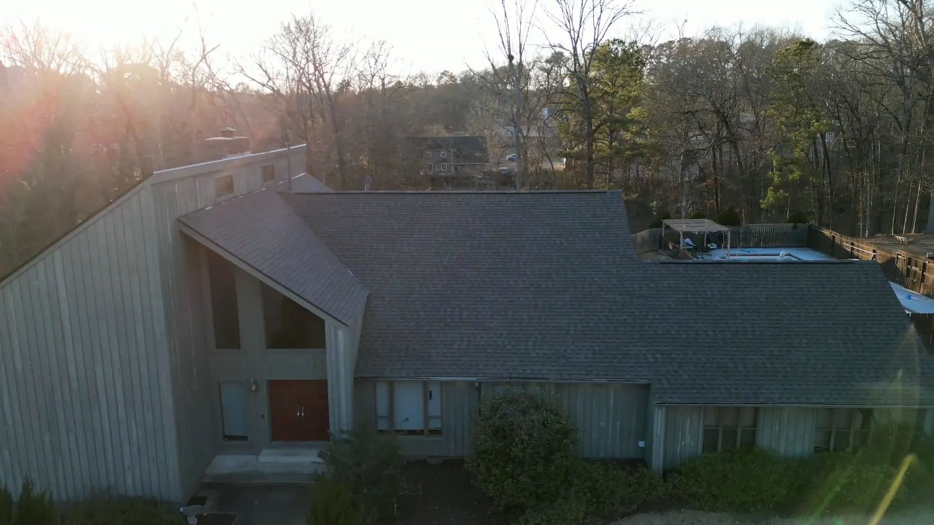 Wood-sided valley home with a new shingle roof surrounded by bare winter timber